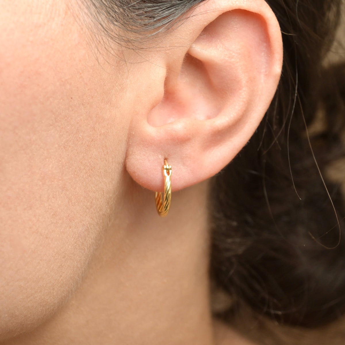Gold hoop earring worn by a person with a neutral background