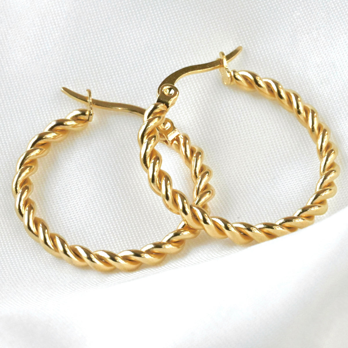 Close up view of gold rope hoop earrings with twisted design on a white background