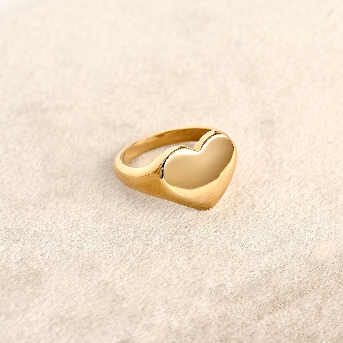 Oversized gold heart statement ring on a light beige background