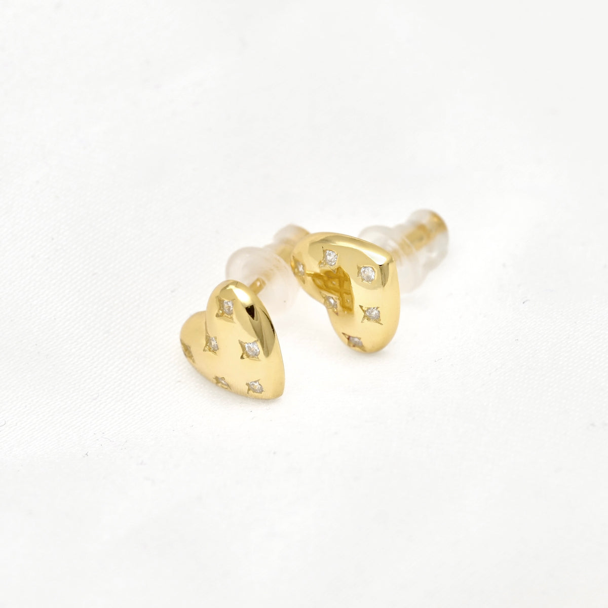 A pair of gold heart-shaped stud earrings with small clear gemstones and silicone backings, shown on a clean white background.