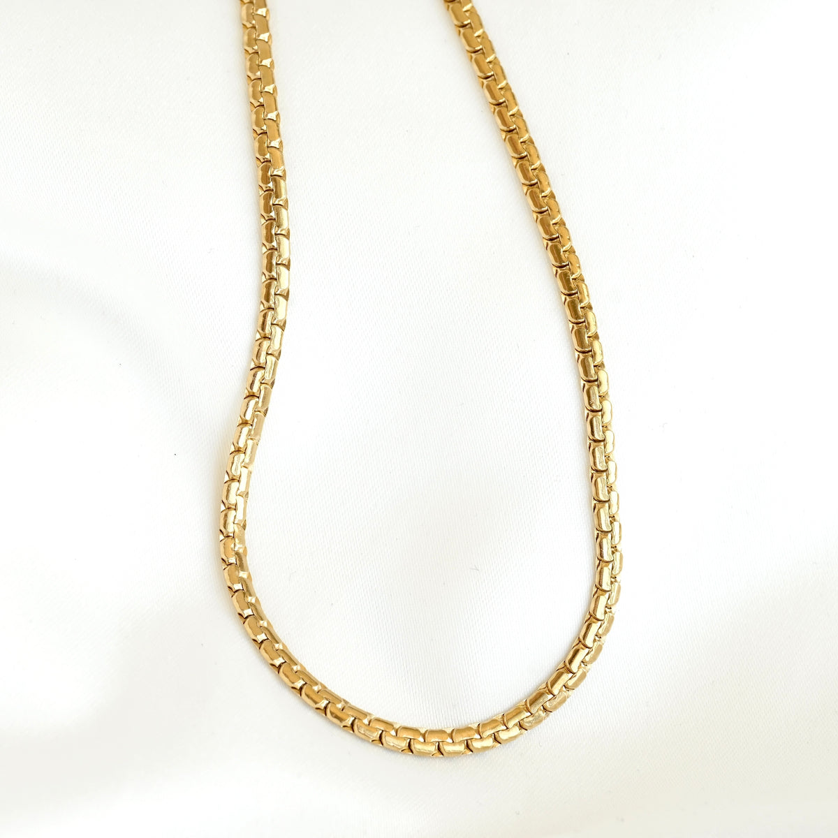 A gold-colored curb link chain necklace, shown draped in a U-shape against a plain white background.