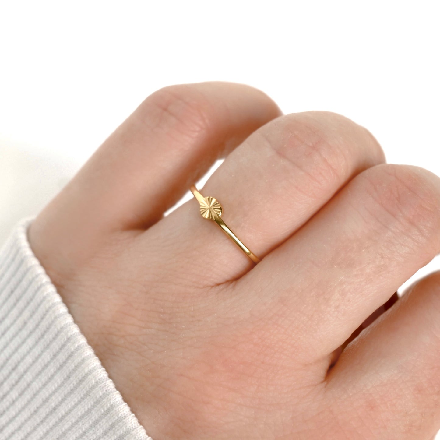 A super simple thin gold ring with a small sunburst or starburst heart-shaped setting, shown worn on a person's finger.