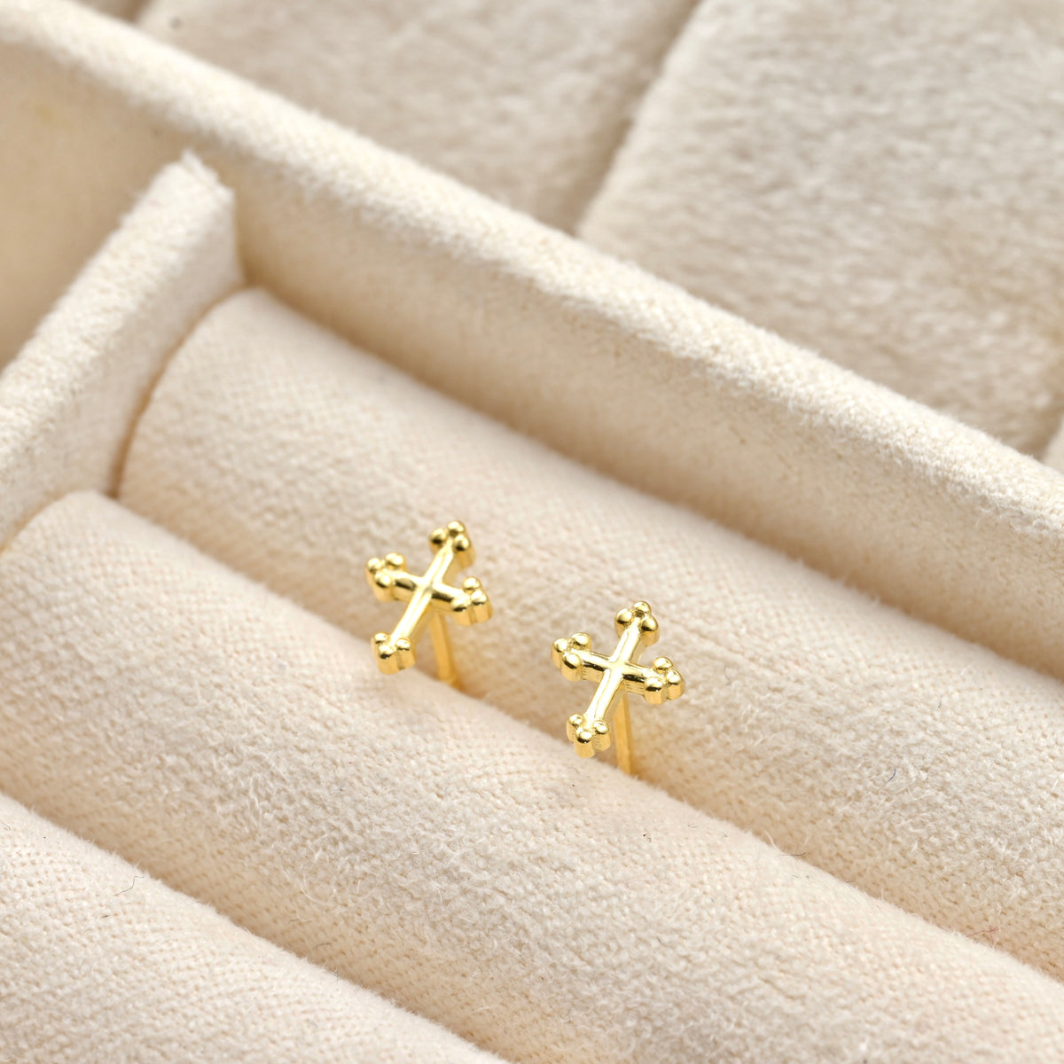 Tiny Gold cross earrings on a textured beige surface