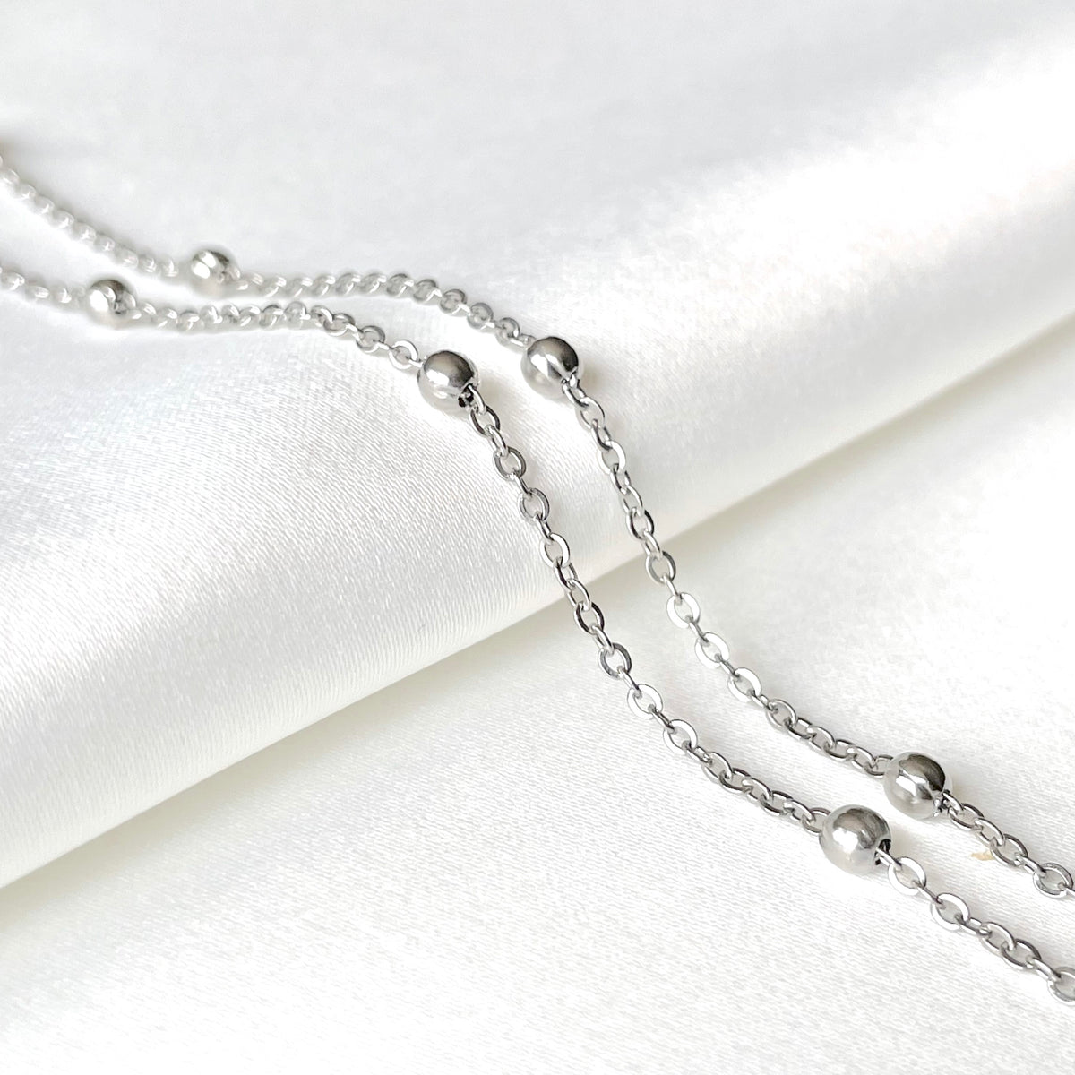 Silver beaded satellite necklace on a white satin background