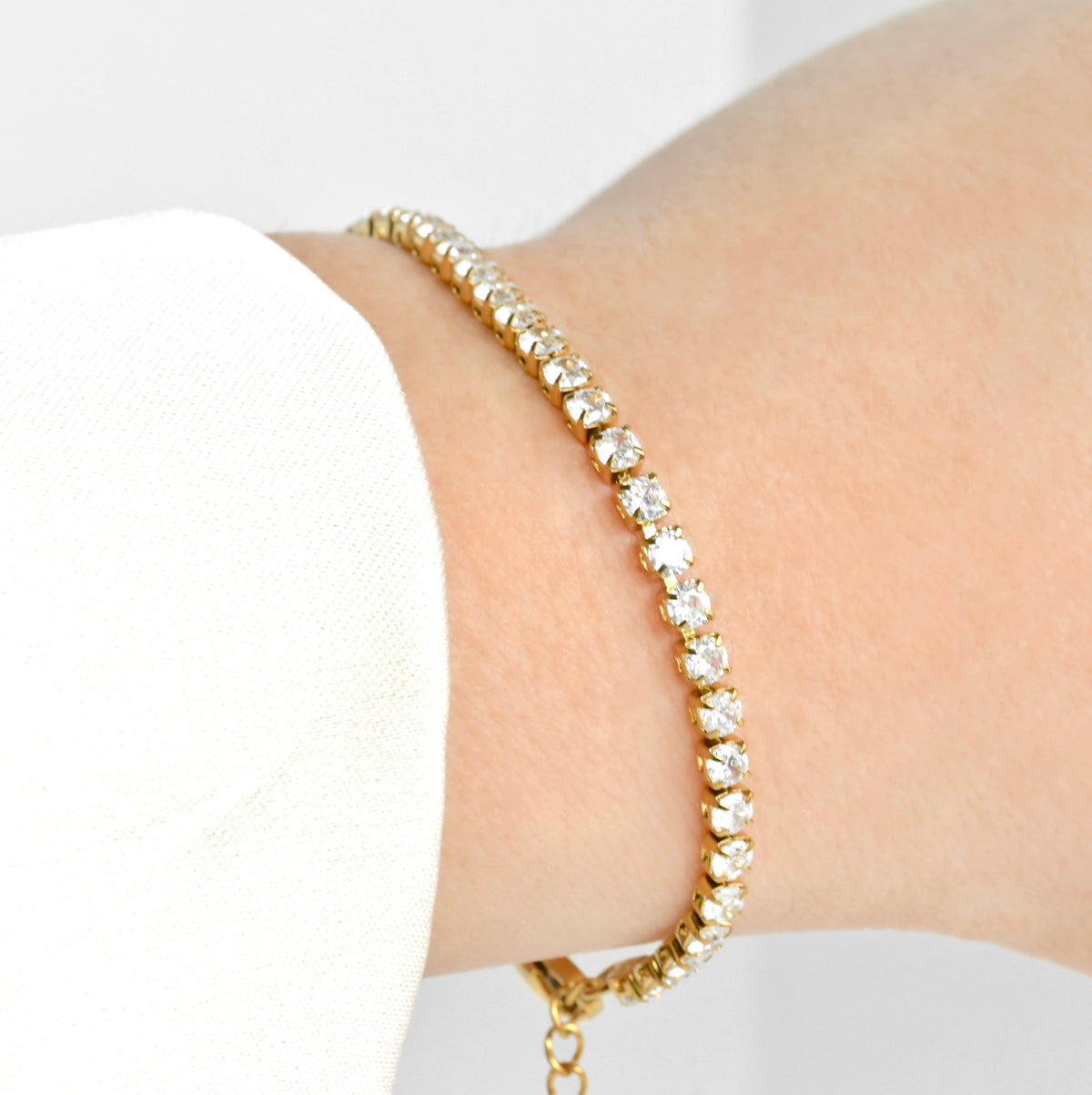 Gold CZ bracelet with clear stones on a wrist against a white background