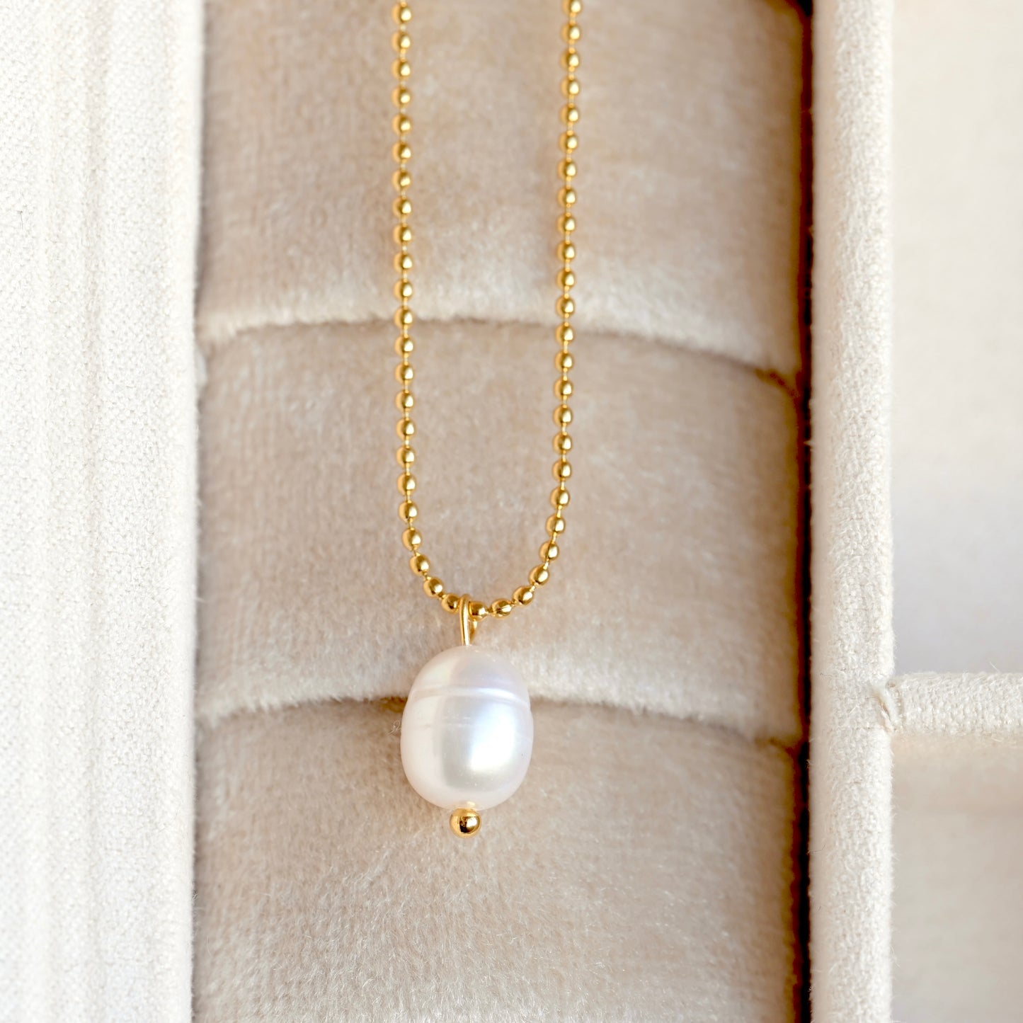 Pearl necklace with gold chain on a textured beige jewelry box