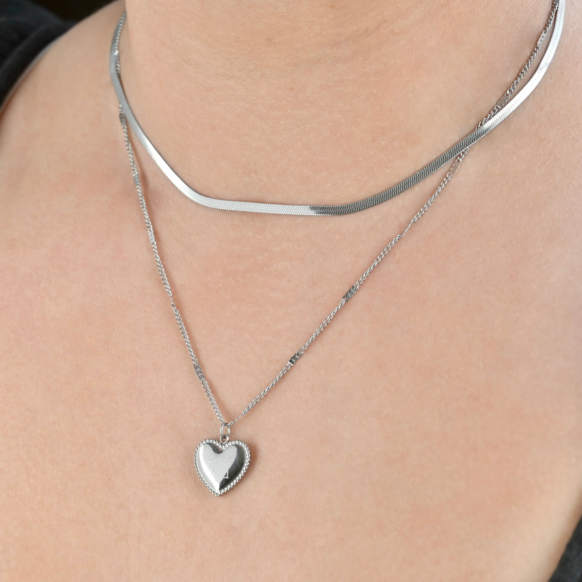 Silver heart-shaped pendant necklace paired with a flat snake chain on a person's neck