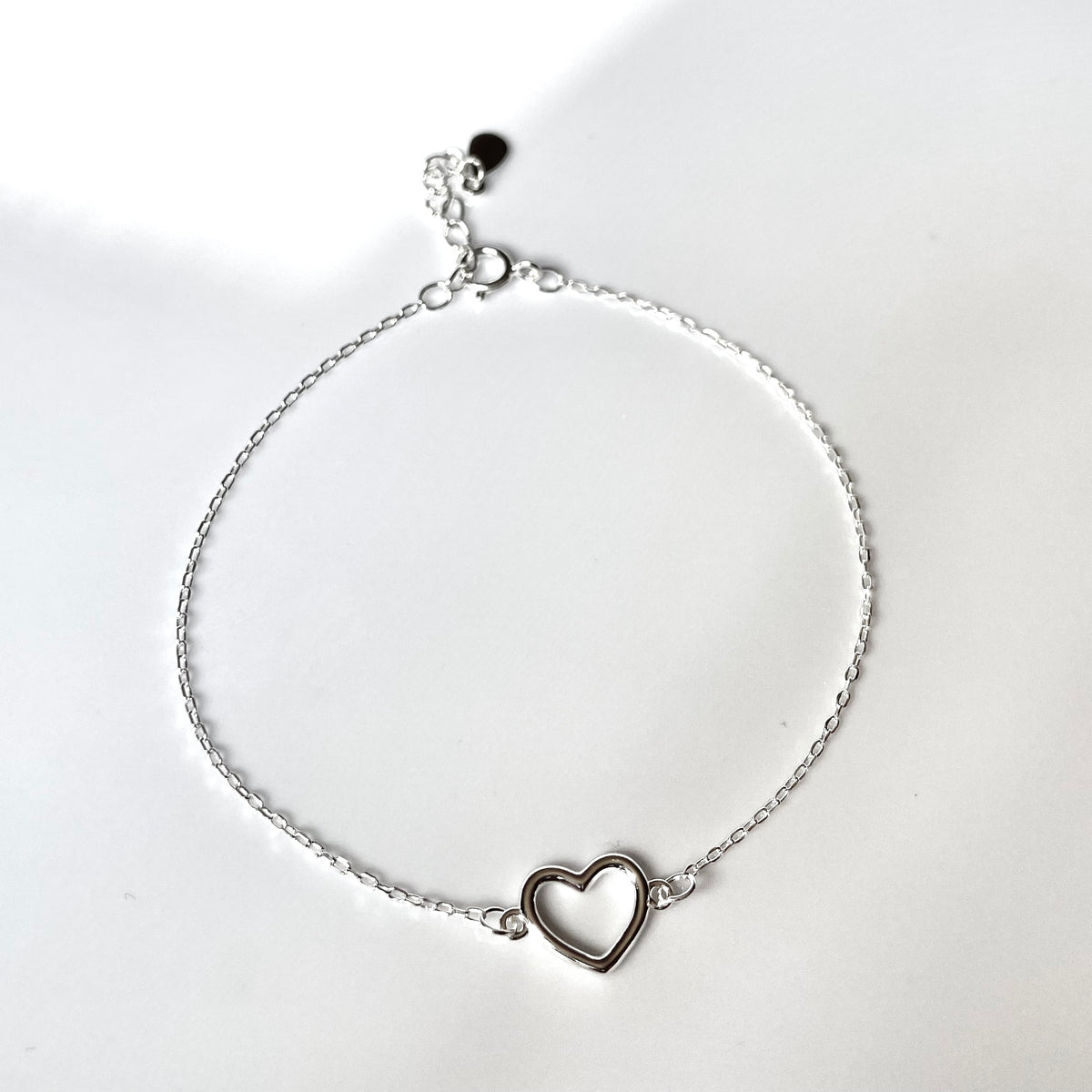 Silver bracelet with a heart charm and a ultra fine cable chain on a white background