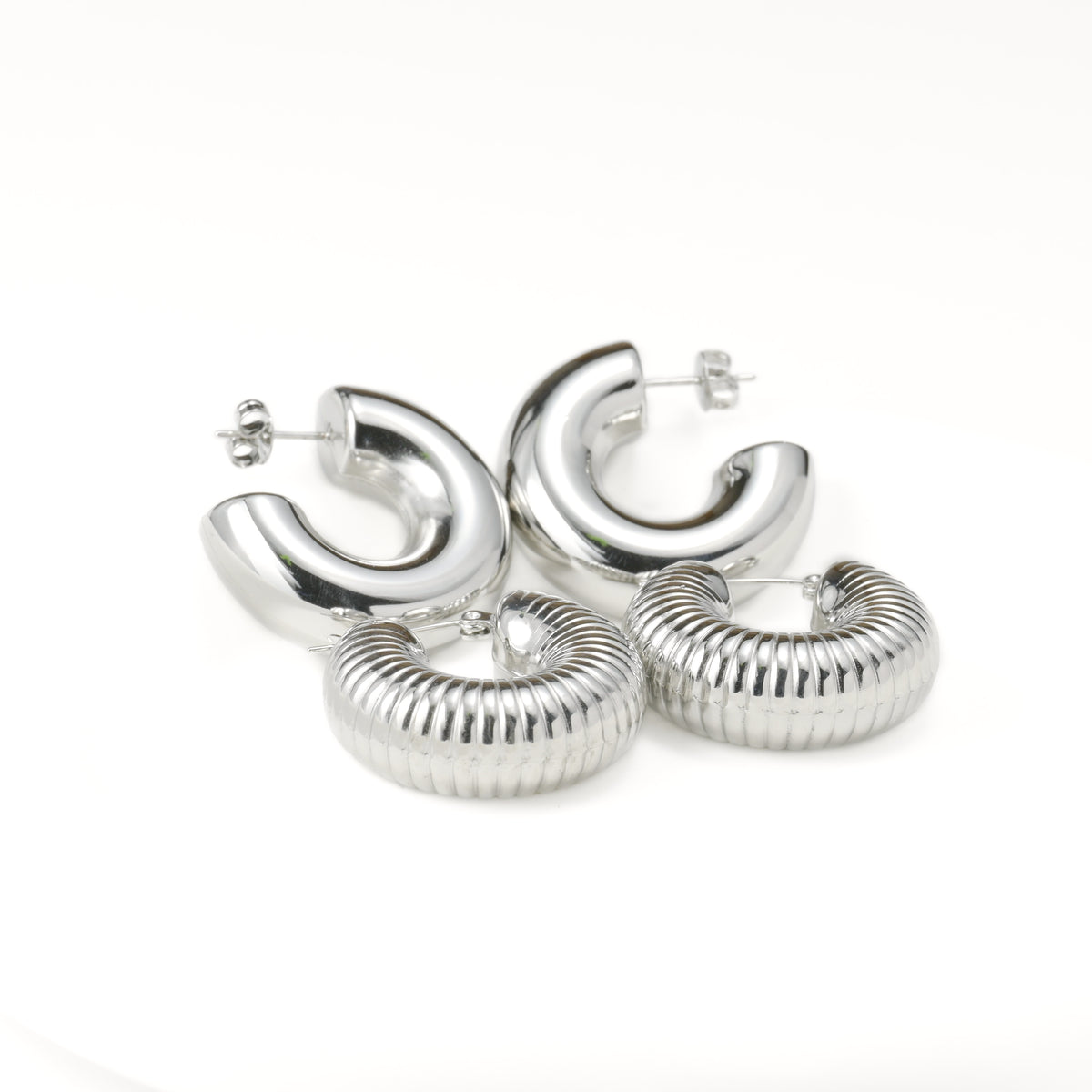 Set of thick silver hoop earrings with plain and textured designs on a white background