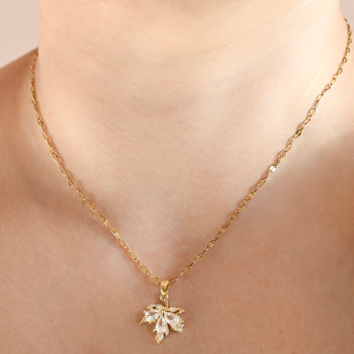 A close-up of a person's neck and collarbone wearing a delicate gold chain necklace with a small flower-shaped clear crystal pendant.