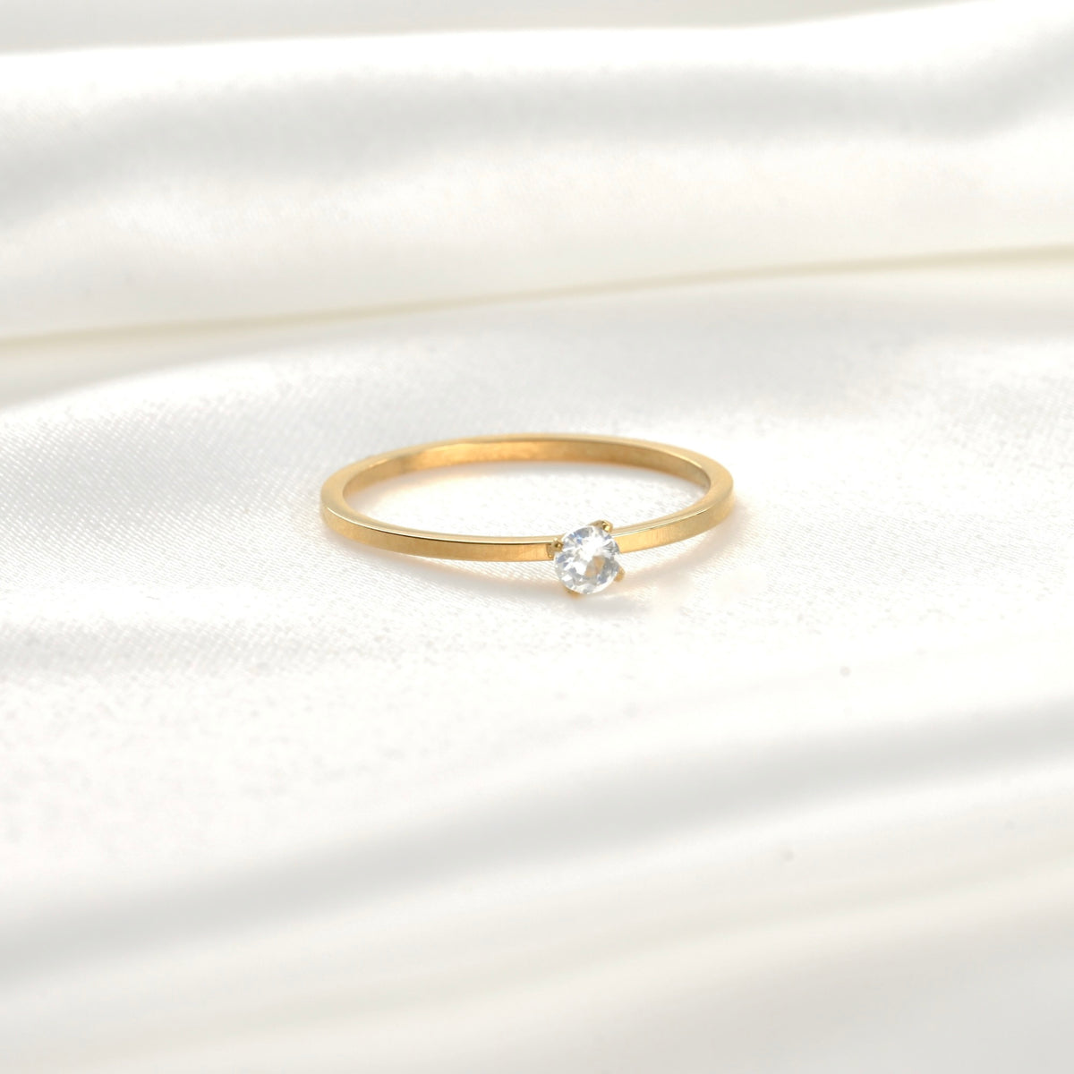 Front view of gold ring with a single small round stone on a white satin background