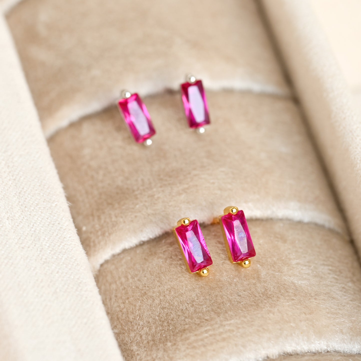Pair of small gold and silver earrings with ruby gemstones on a beige fabric background