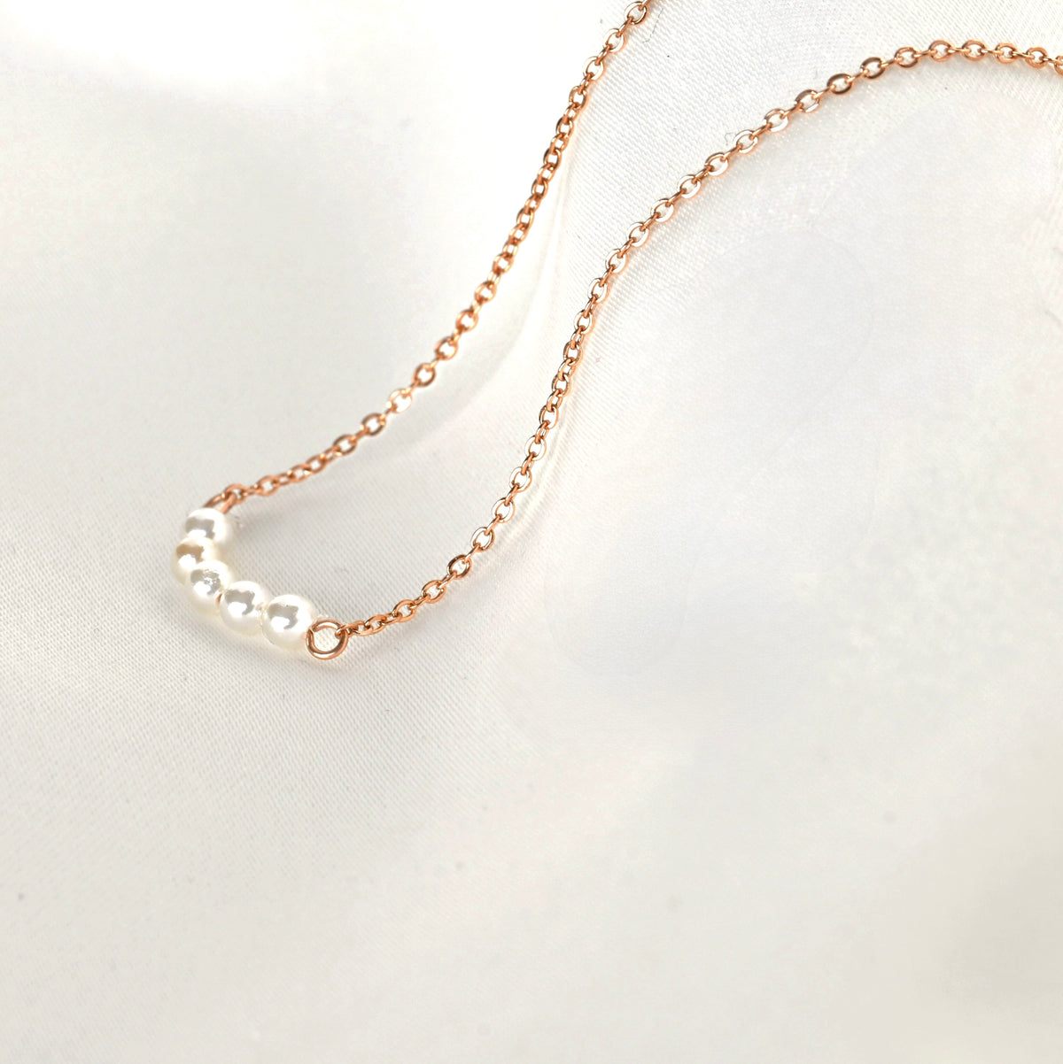 Close up side view of rose gold necklace with 5 tiny pearls forming a small curve on a light gray background