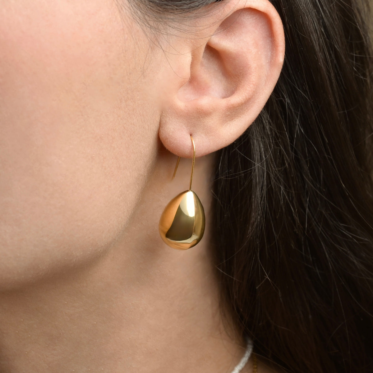 Gold teardrop earring with a hook worn by a person