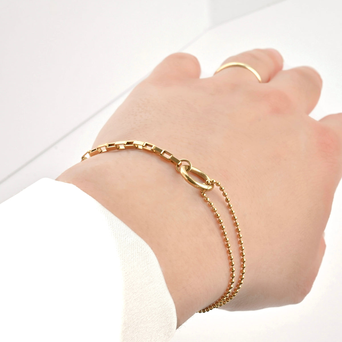Gold chain bracelet on a wrist with a plain background