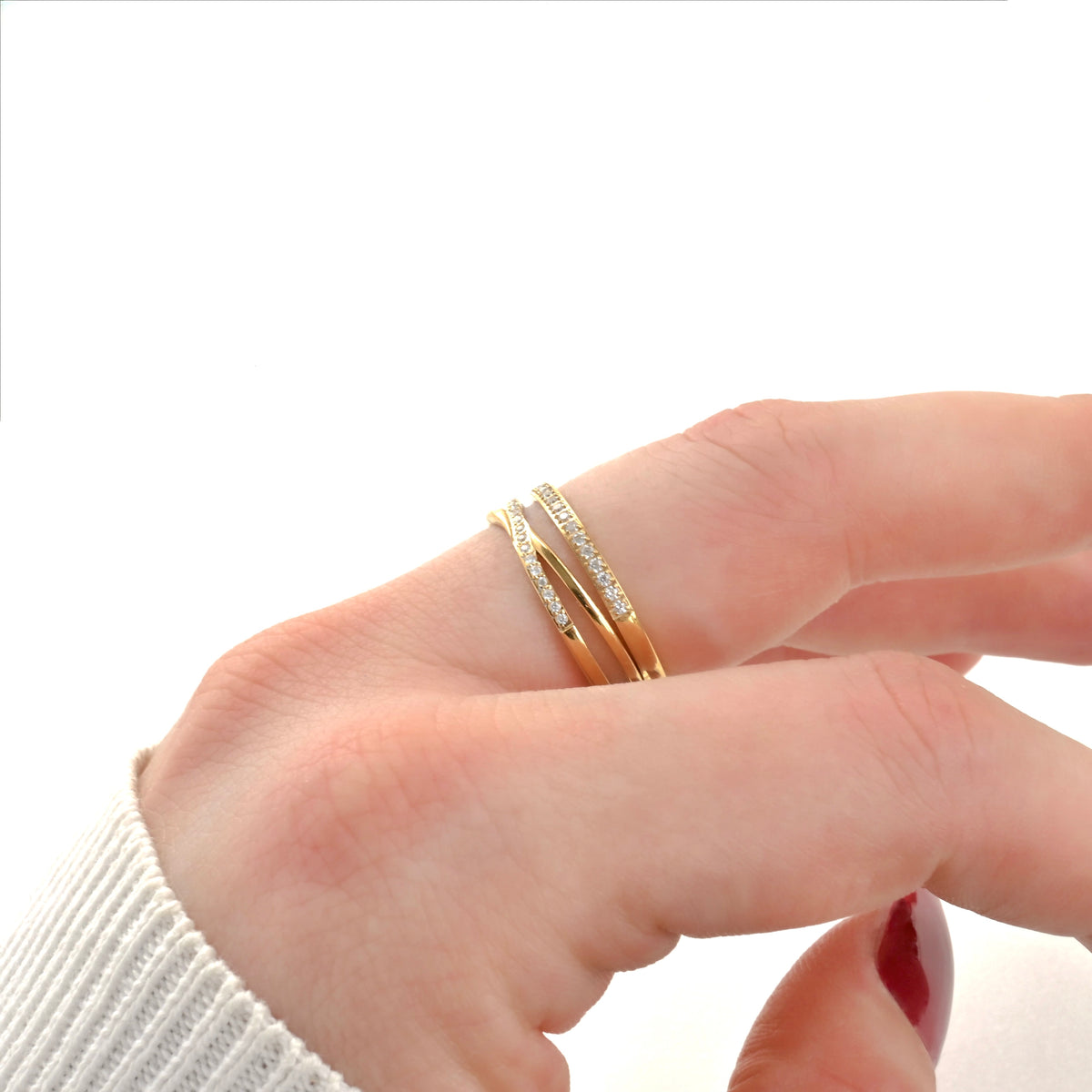 Hand wearing an X ring and a matching slim band stacked on top with a white background