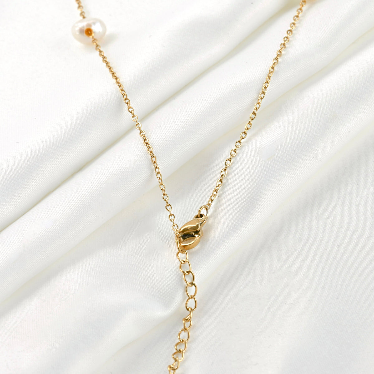 Close up view of the lobster claw clasp and extender of gold pearl chain necklace on a white fabric background
