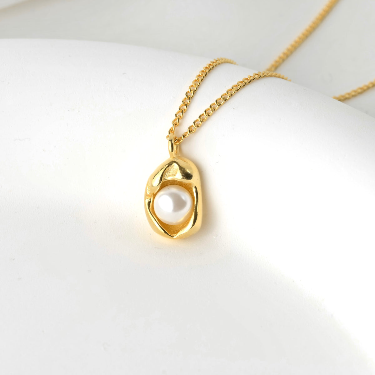 Gold necklace with a pendant featuring an oyster shell holding a white pearl.