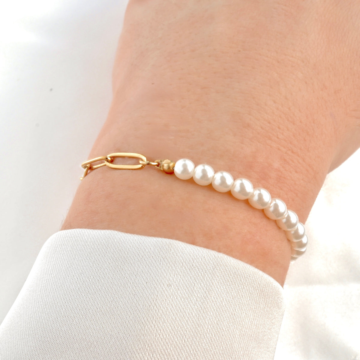 Half pearl half paperclip bracelet on a wrist with a gold toggle clasp against a white background