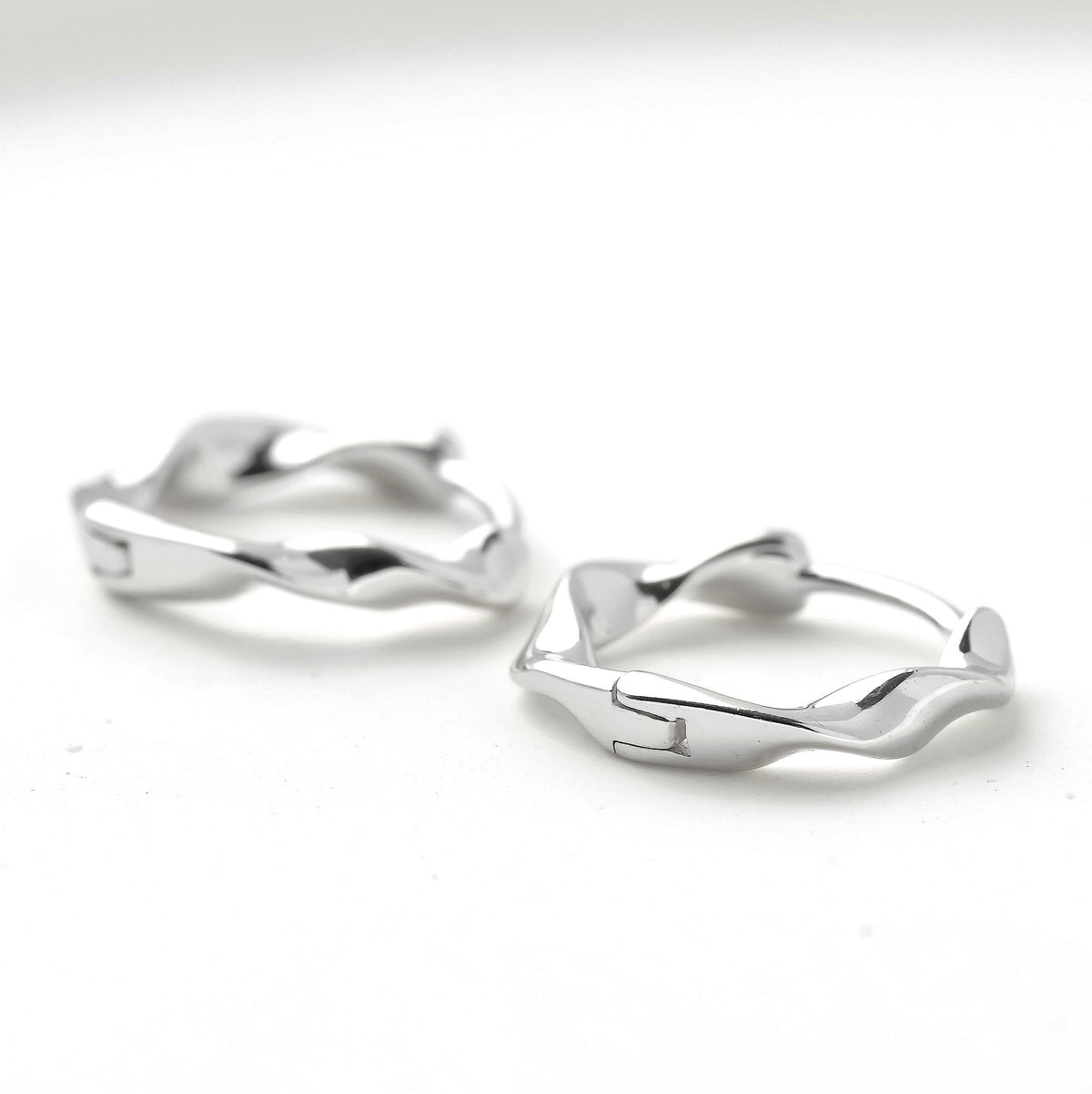 Pair of silver huggie earrings with hinged closure on a white background