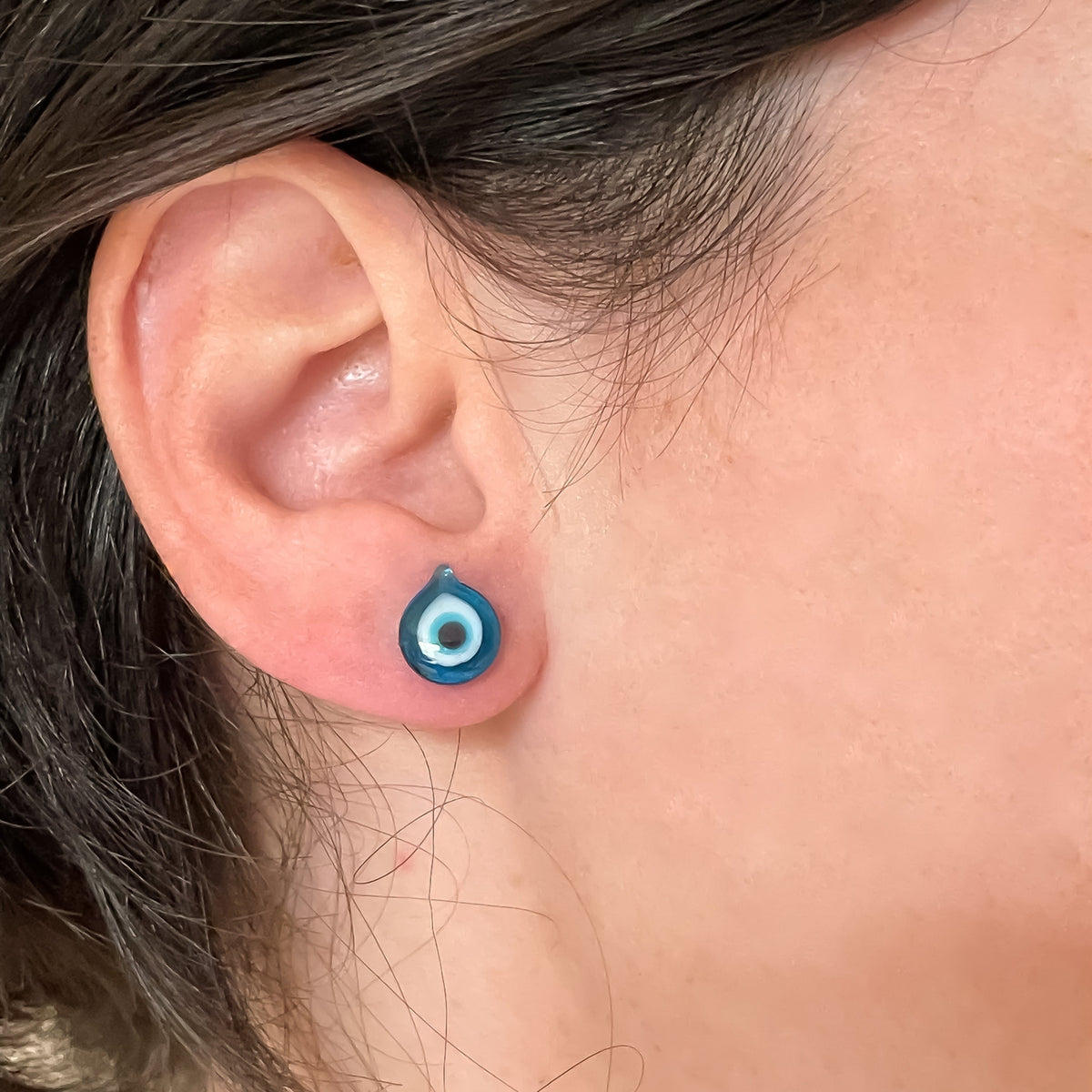 Close-up of an ear with teardrop-shaped light blue eye stud earrings