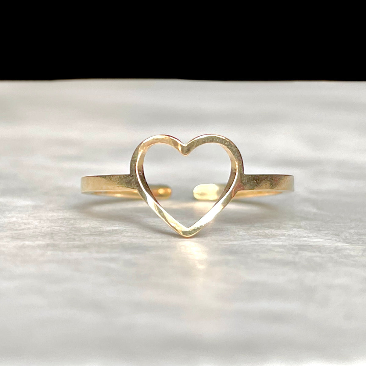 Front view of gold heart ring with the open back side is seen through the center of heart charm on a light gray background