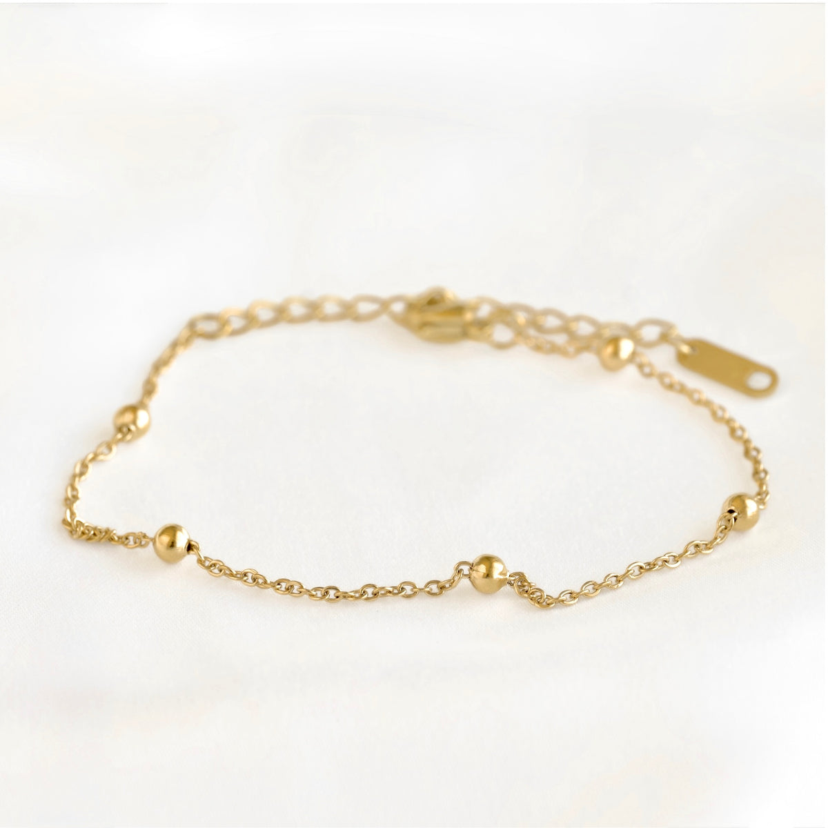 A delicate gold chain bracelet with small polished gold bead accents, displayed on a soft white background.