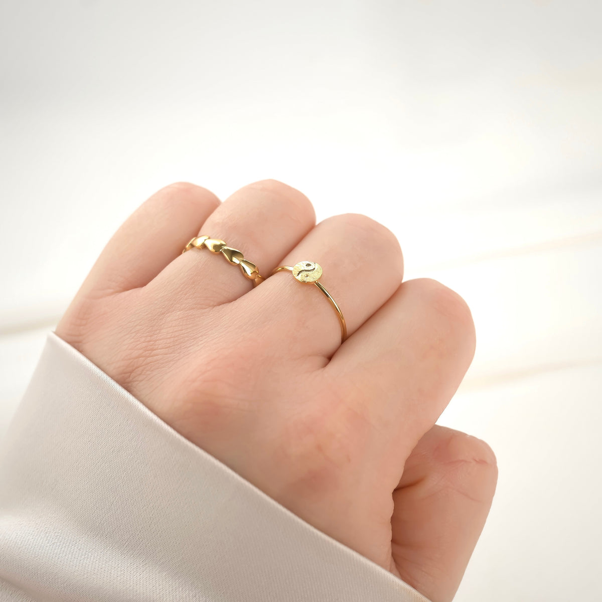 Gold taijitu ring on a finger against a white background