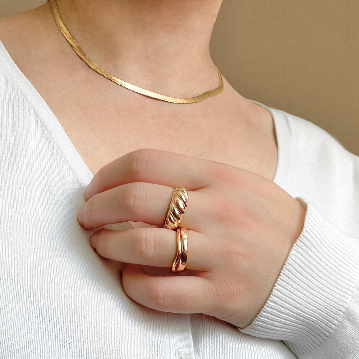 Close-up of a hand wearing a croissant ring and stacked gold wave rings with a blurred background