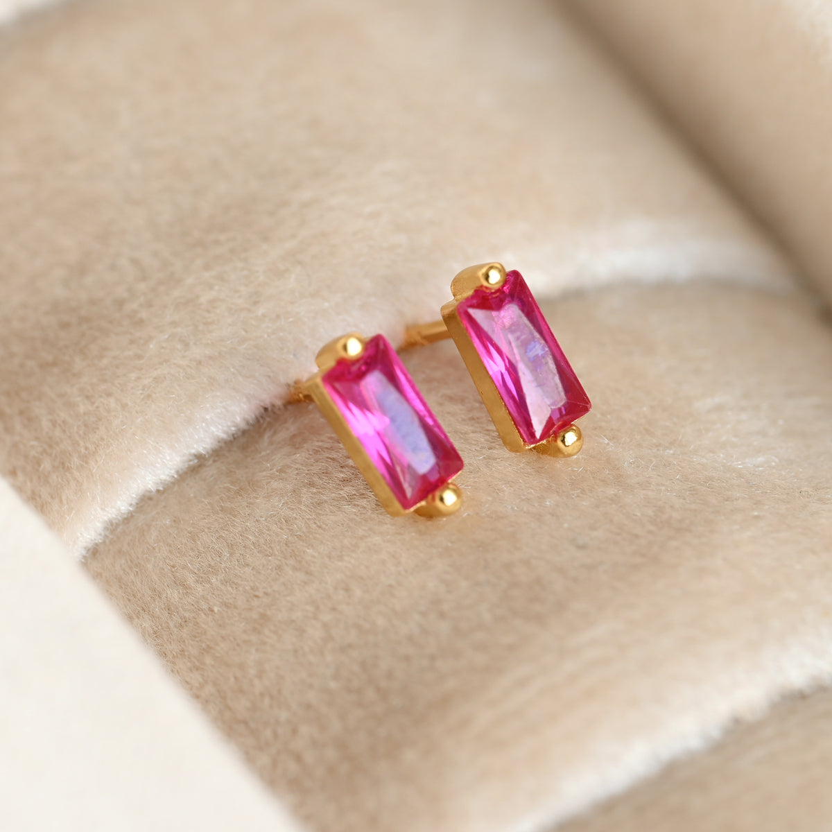 Gold earrings with pink gemstones on a beige fabric background