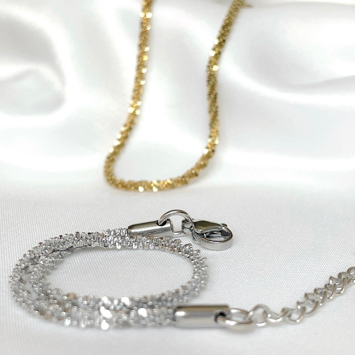 Sparkling chain bracelets in gold and silver on a white satin background