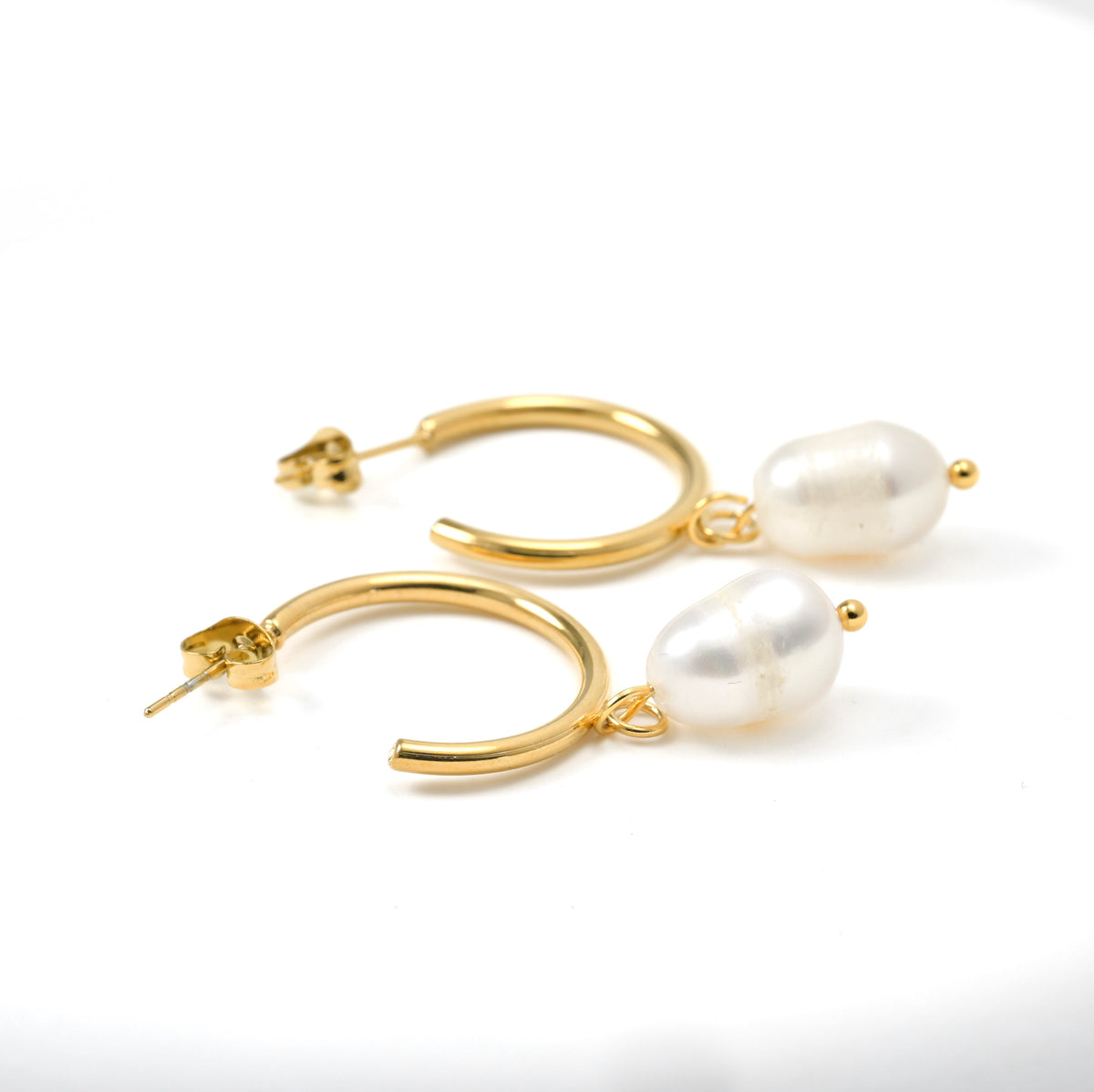 Dainty gold hoop earrings with white oval pearls on a white background