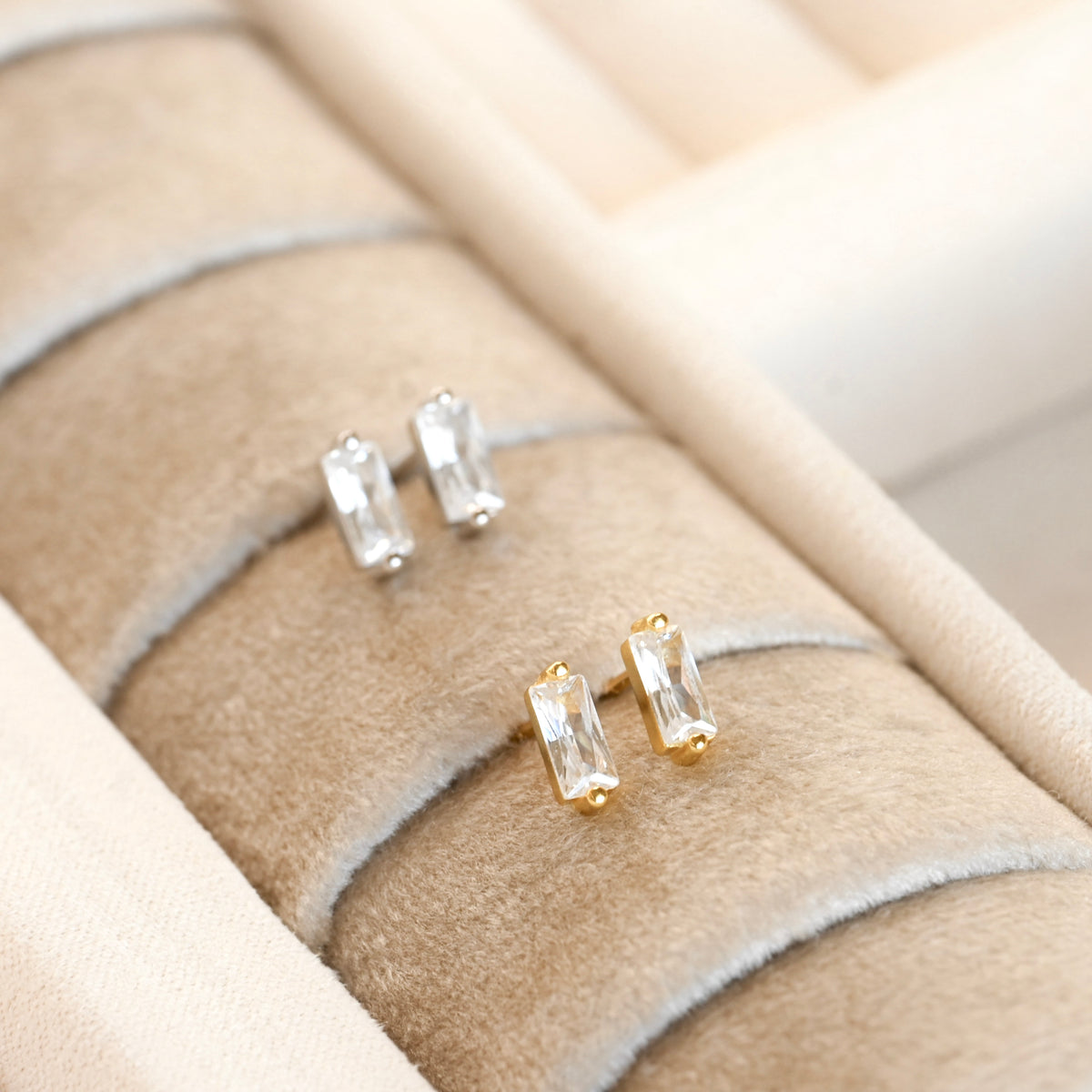 Gold bar earrings with clear stones on a beige jewelry display