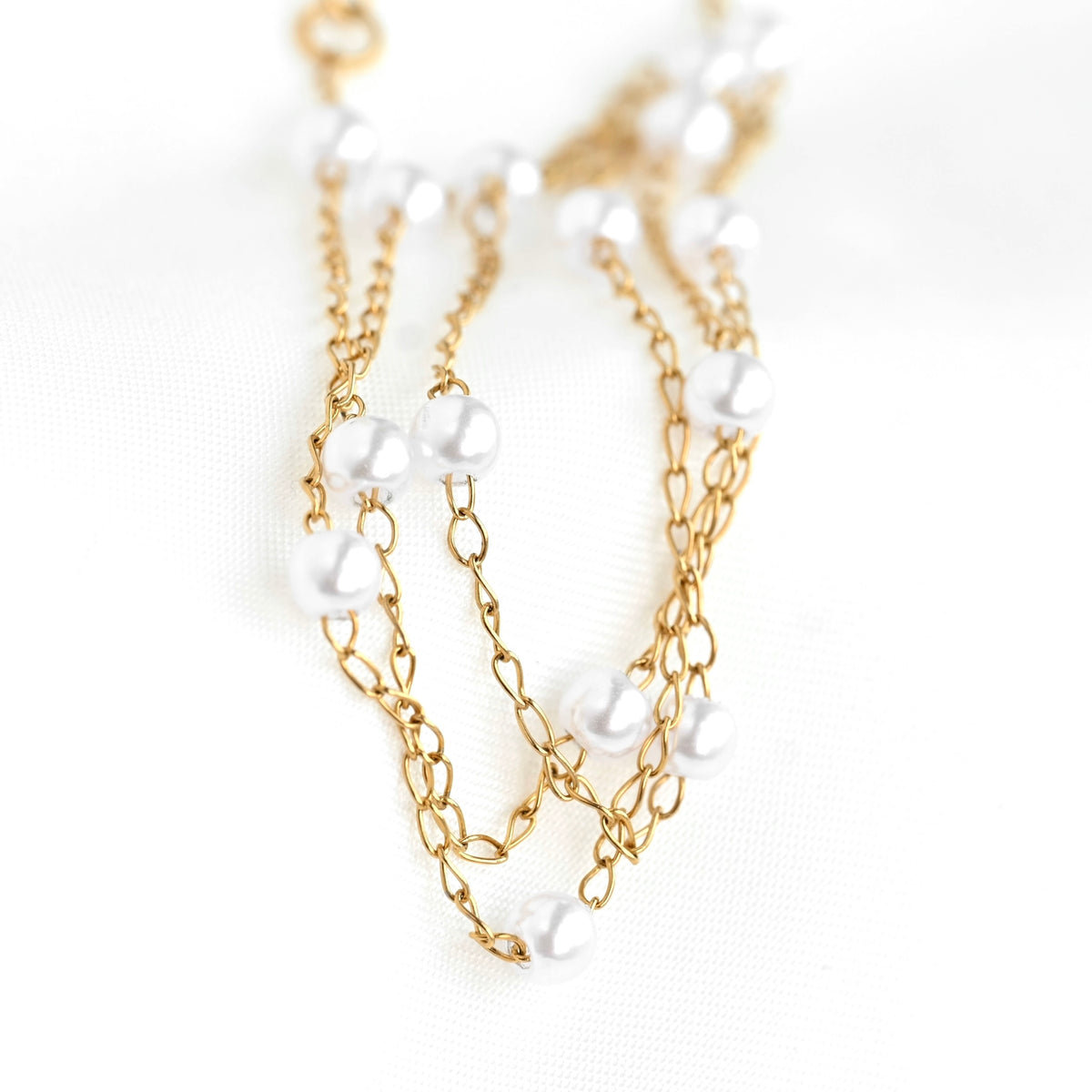 Gold chain necklace with white pearl beads on a light background