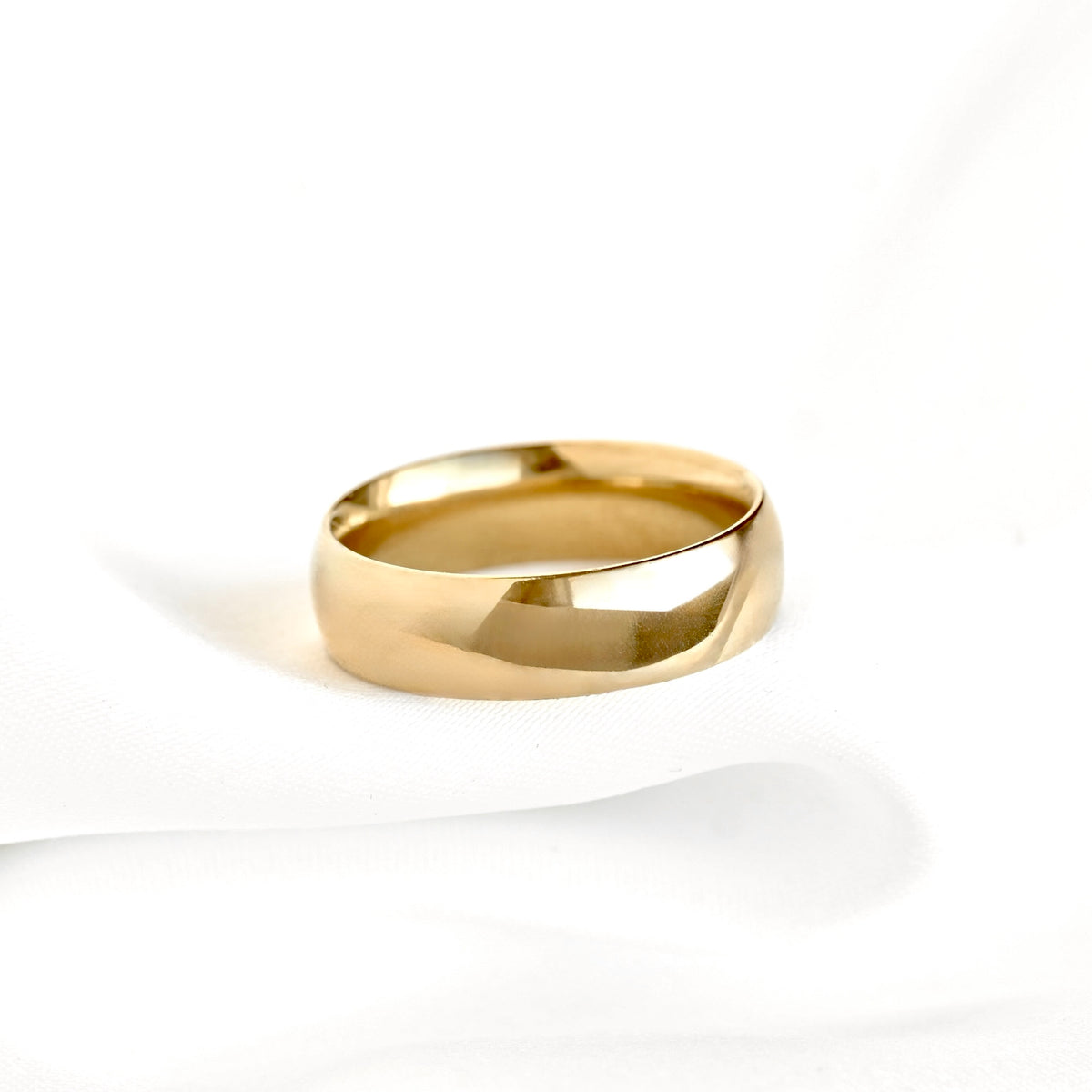 A thick and wide polished yellow gold band ring with a smooth dome profile, resting on a white textured fabric background.