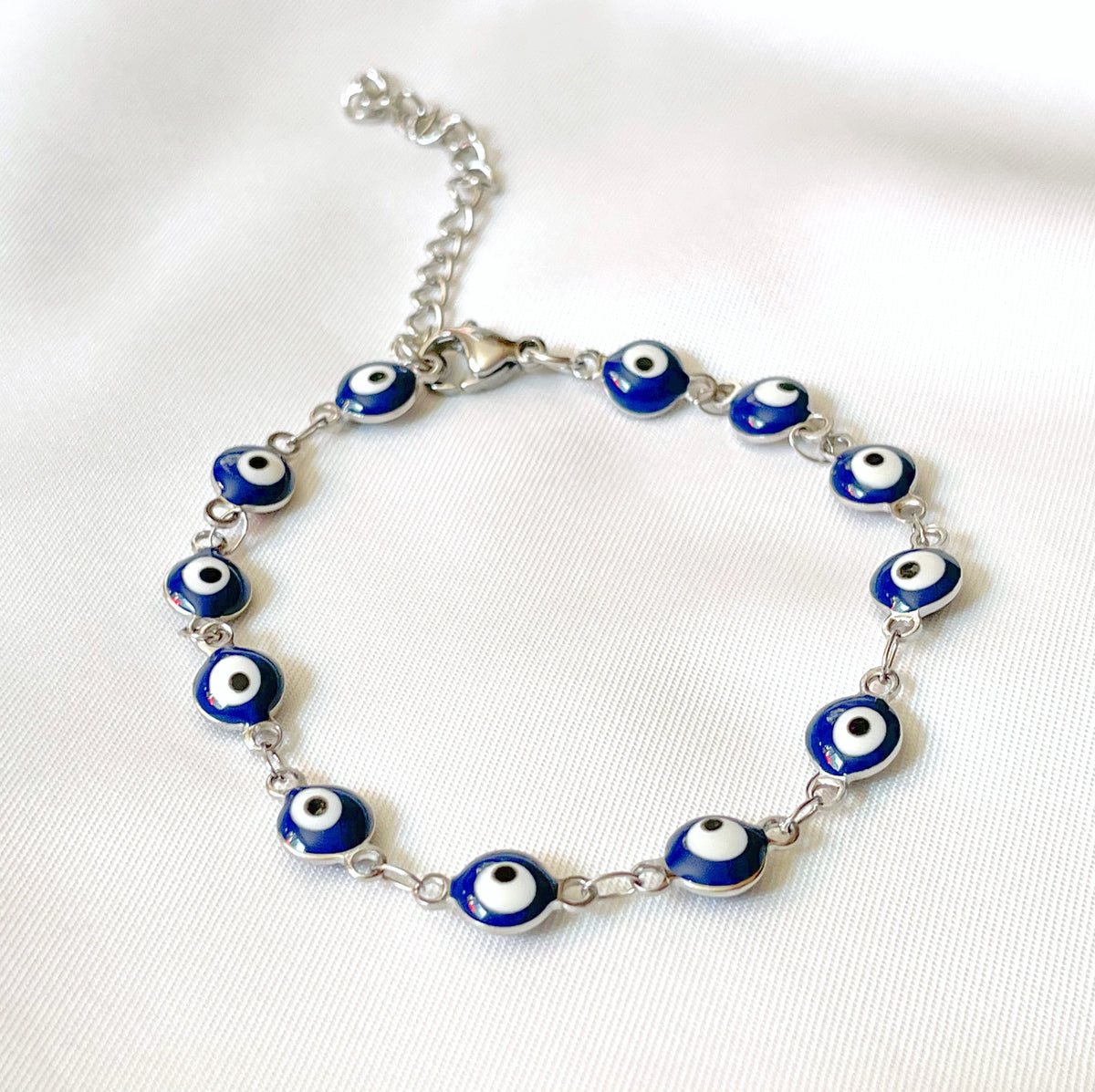 Silver bracelet with blue evil eye beads on a white fabric background
