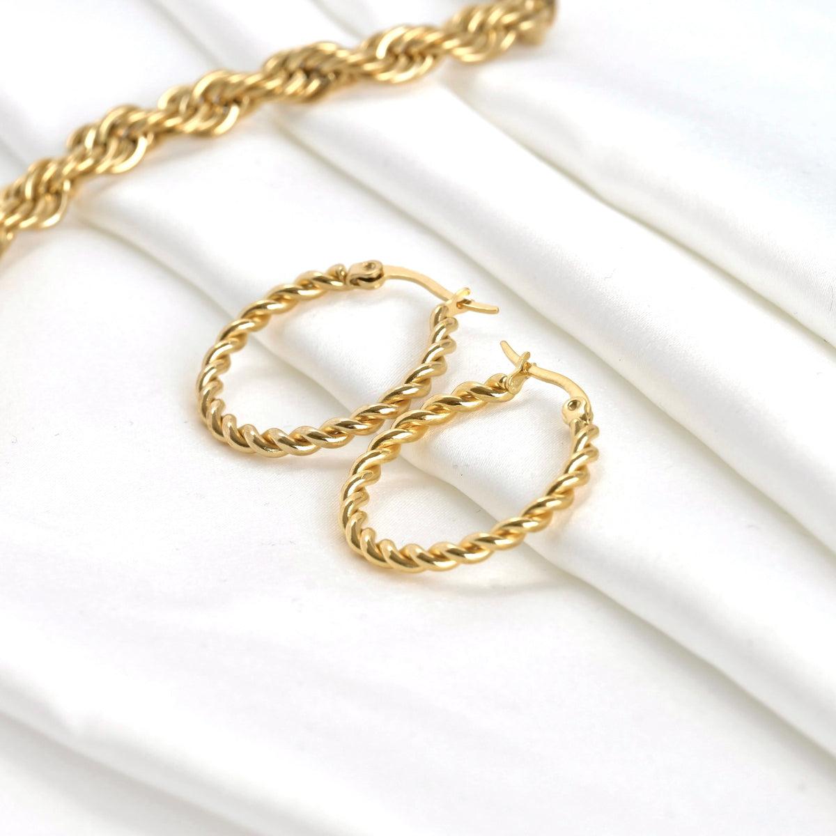 Thin gold hoop earrings on a white background with a thick rope chain in the corner