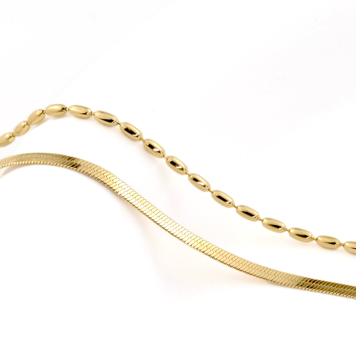 Gold herringbone chain and oval beaded chain on a white background