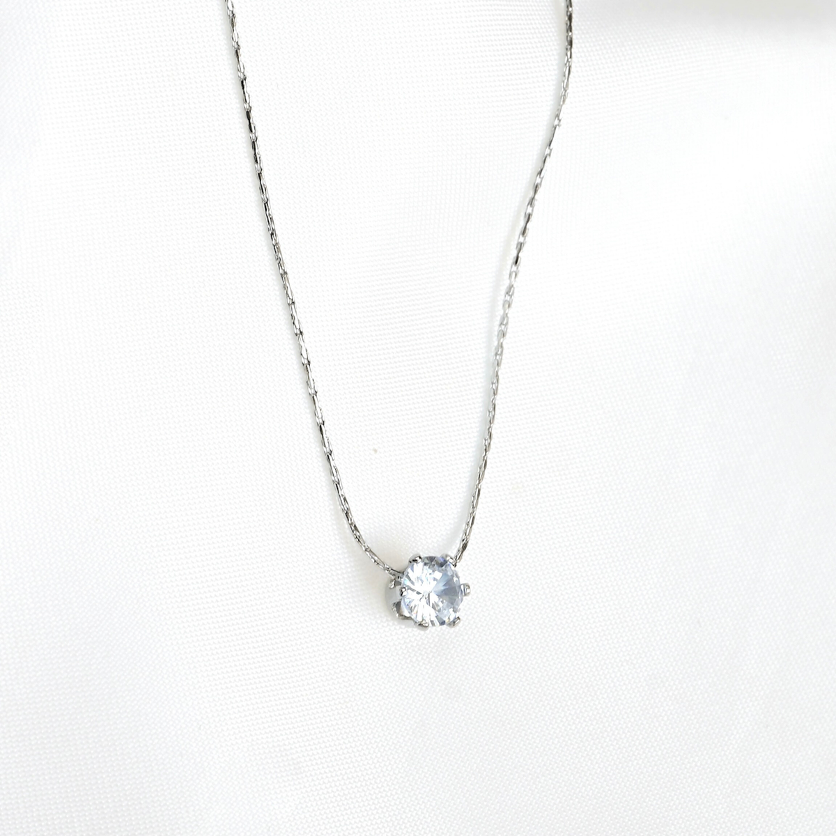 Front view of silver necklace with a round CZ pendant on a white background