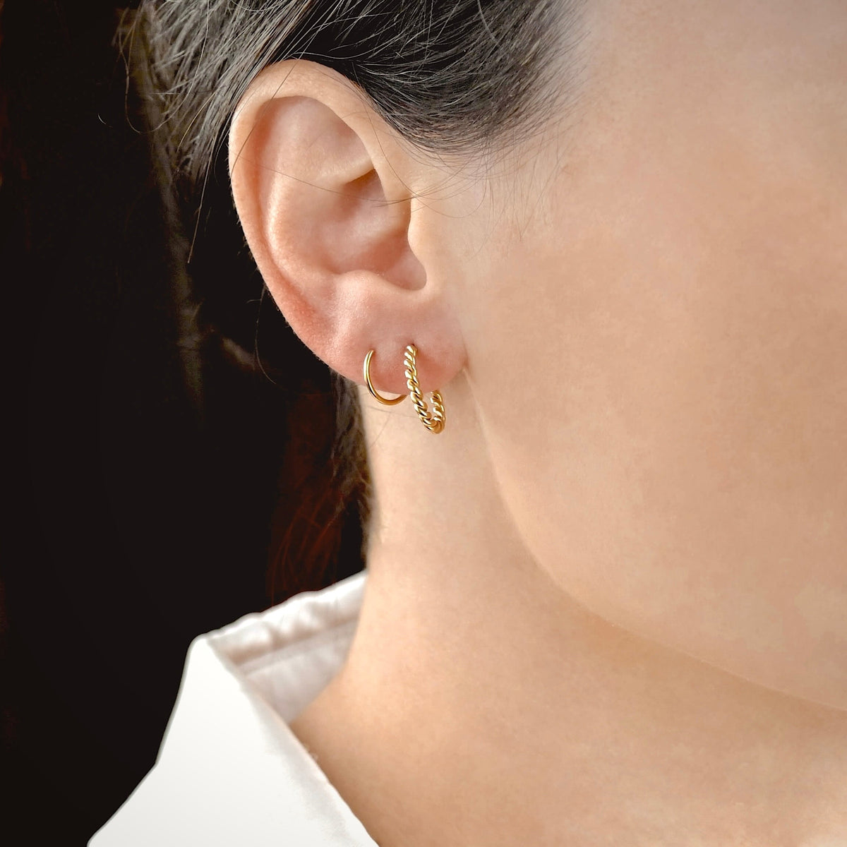 Close-up of a person wearing gold twisted spiral hoop earrings with a blurred background