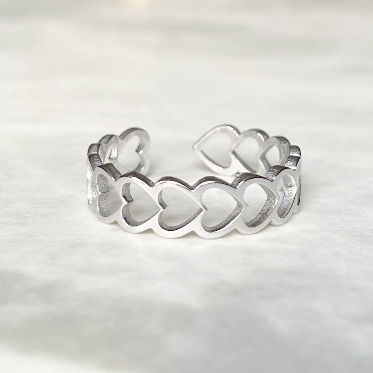 Front view of open back silver heart ring on a light gray background