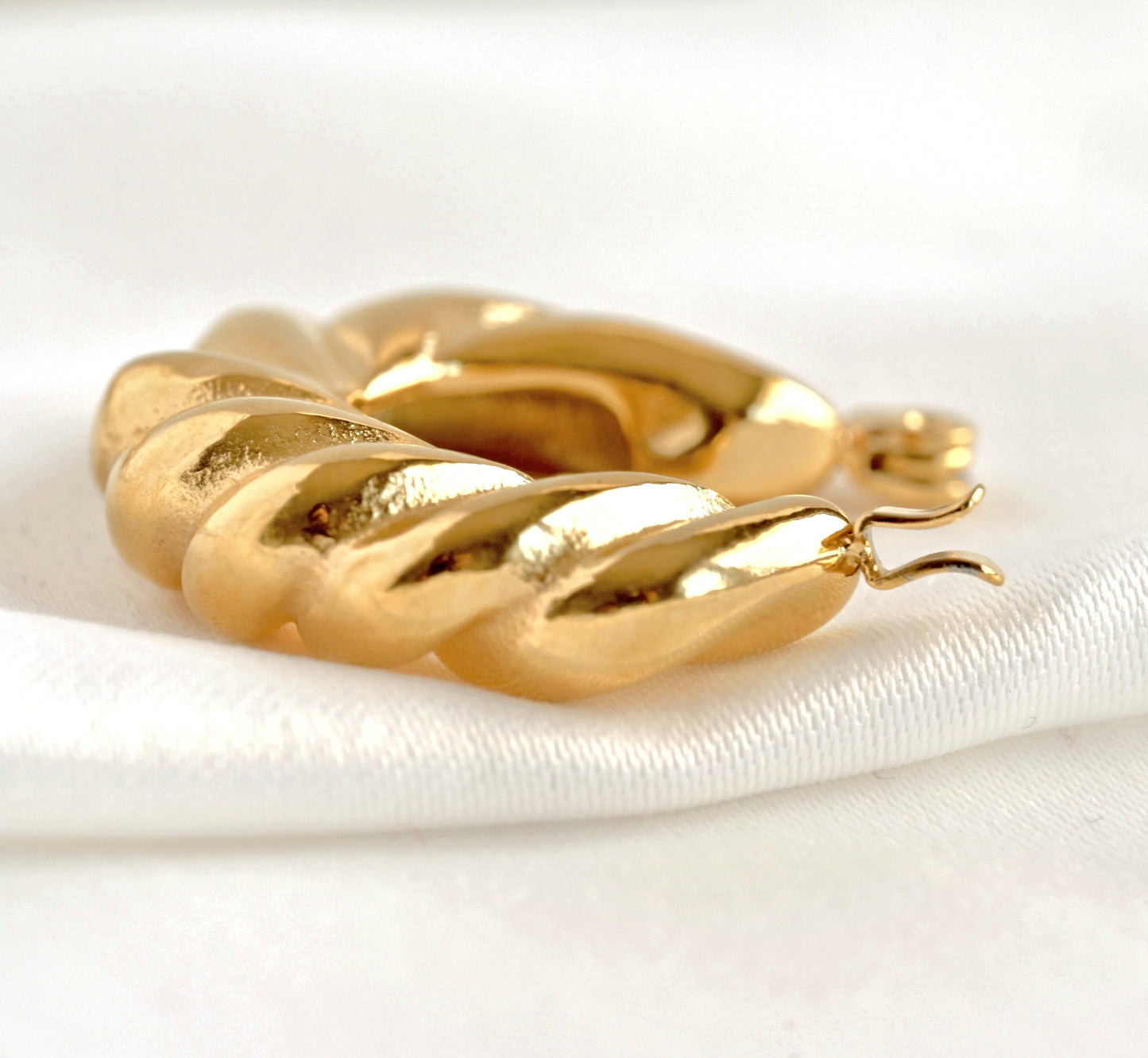 Close-up view of gold hoop earringwith a zoom in to latch back closure on a white satin surface