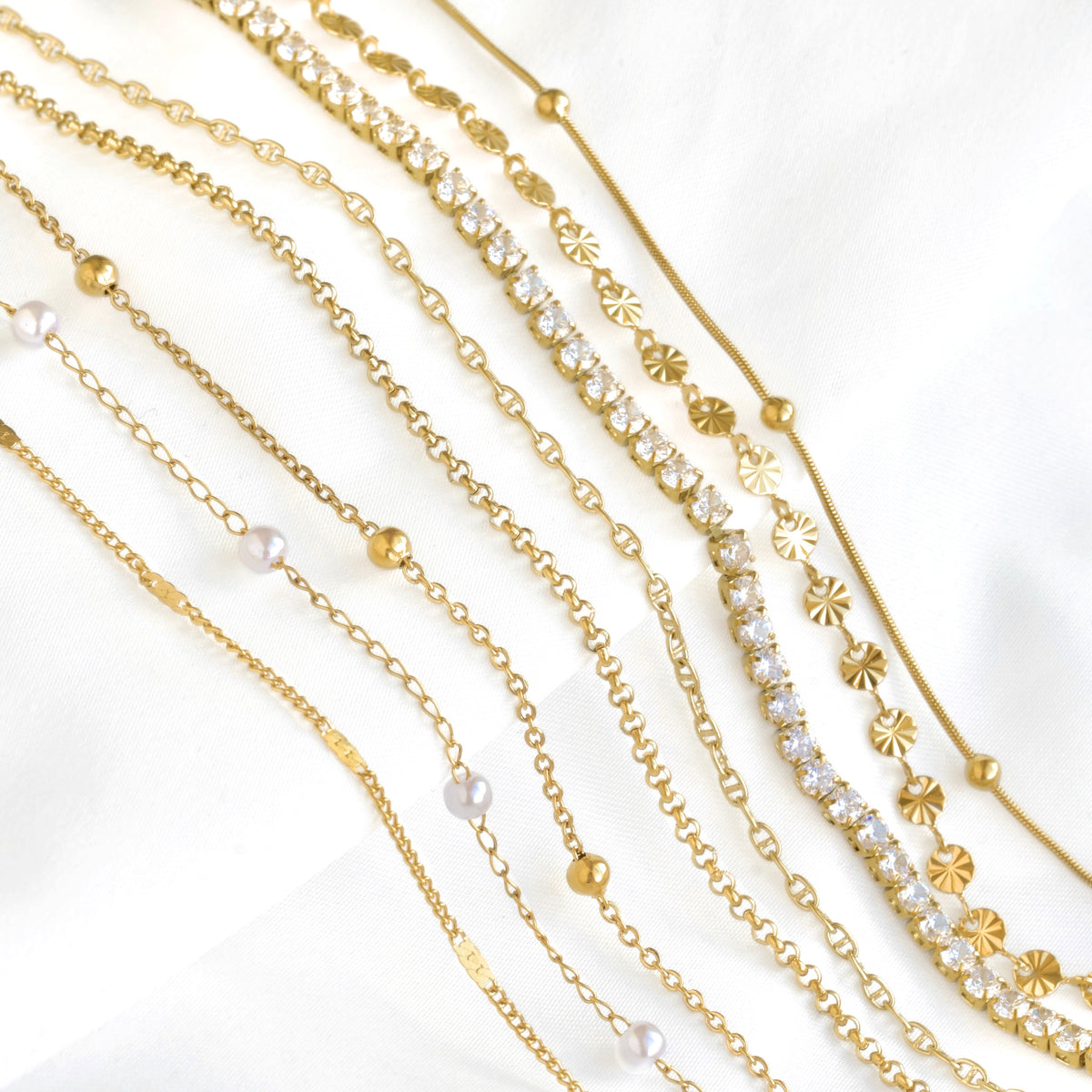 A close-up of delicate gold bracelets placed diagonally on white satin