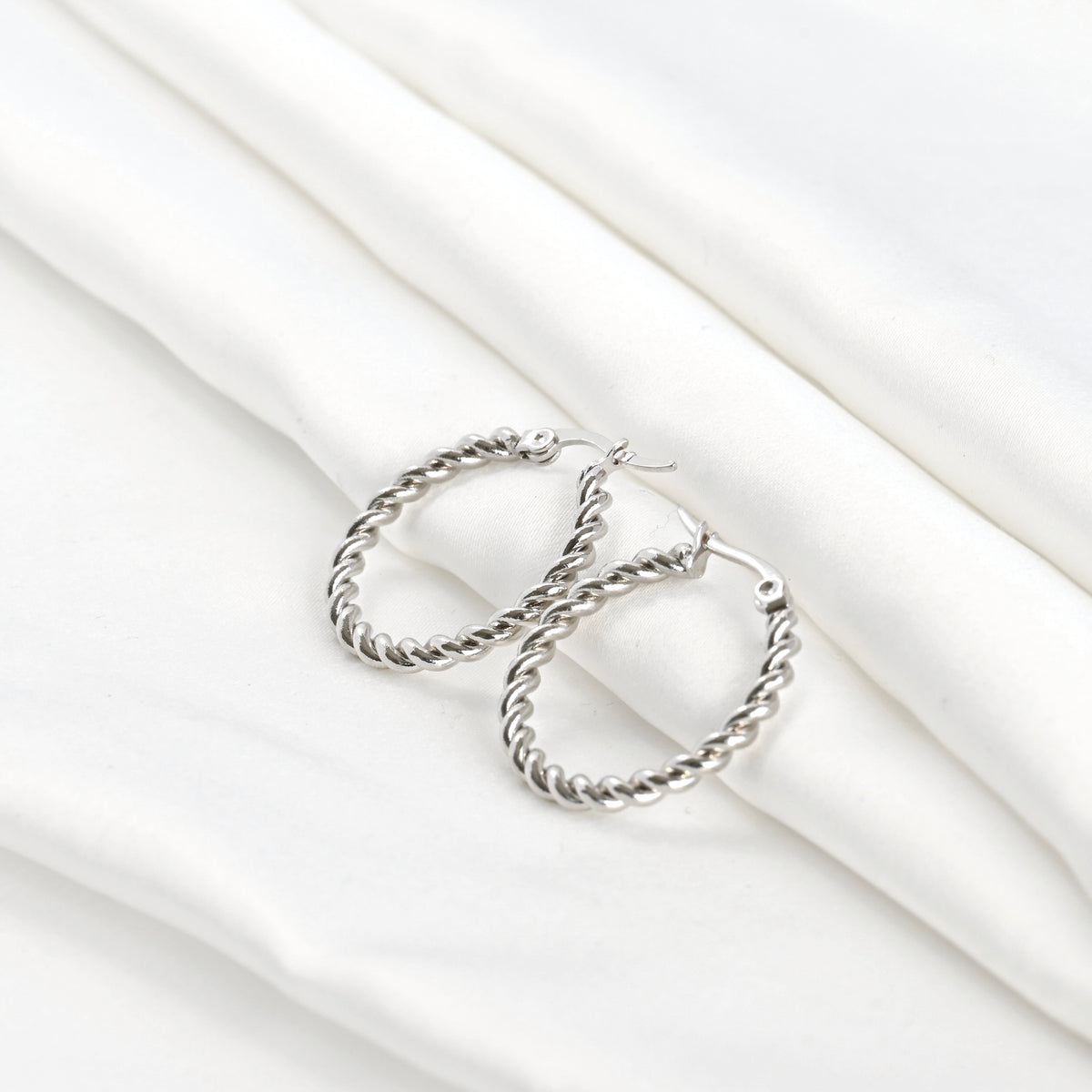 Wide angle view of silver twist hoop earrings on a white fabric background