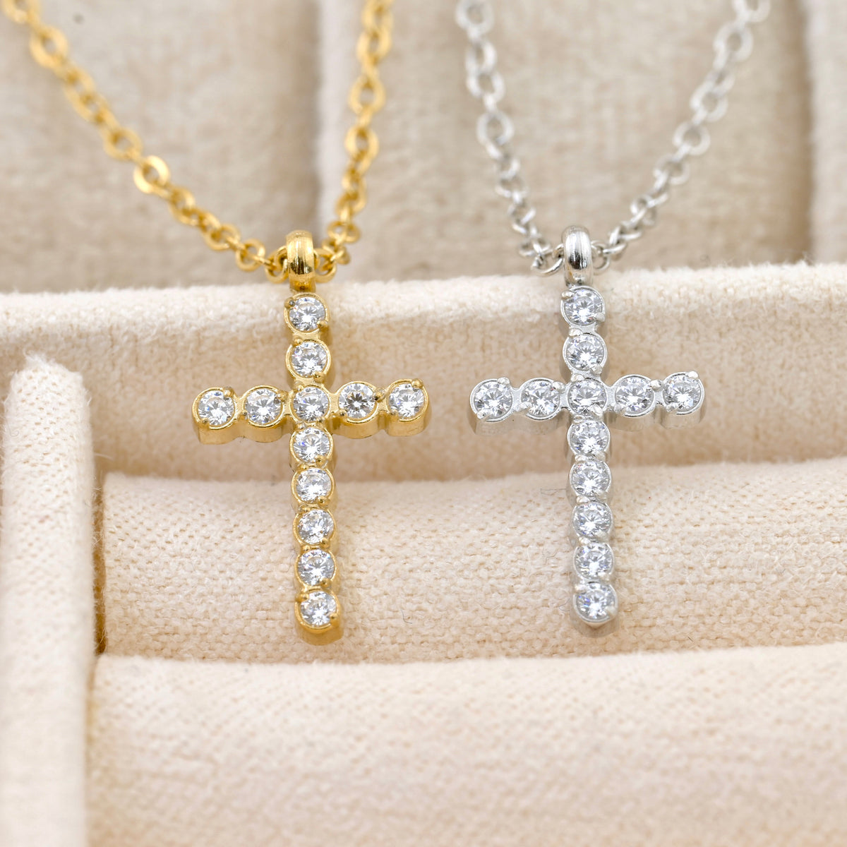 Gold and silver diamond cross necklaces with clear stones on a beige surface