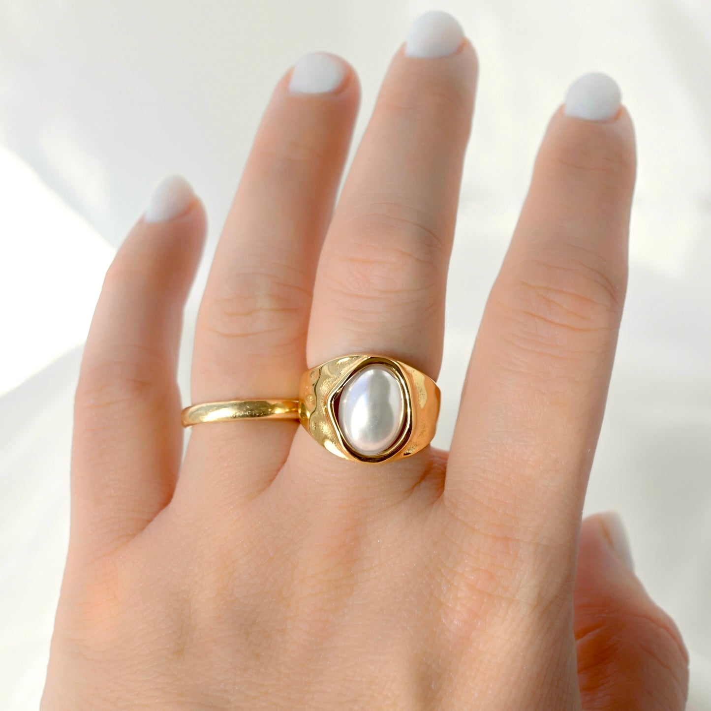 Front view of a a chunky gold pearl ring worn on a person's finger against a soft white fabric background.