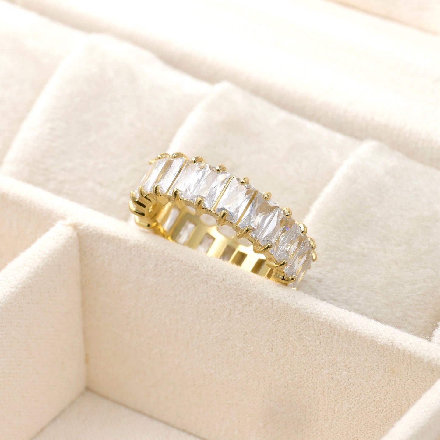Gold eternity band with white diamonds on a beige quilted surface