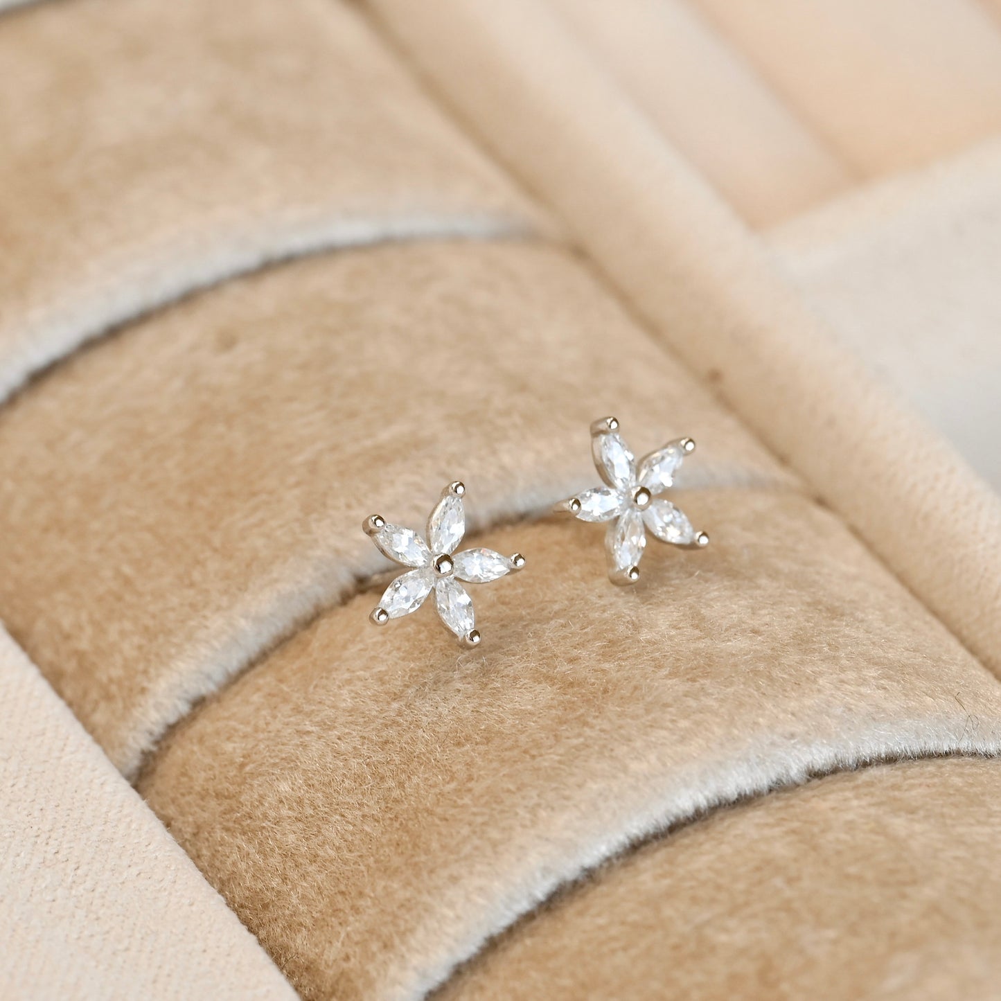 Pair of silver flower-shaped earrings on a beige fabric background