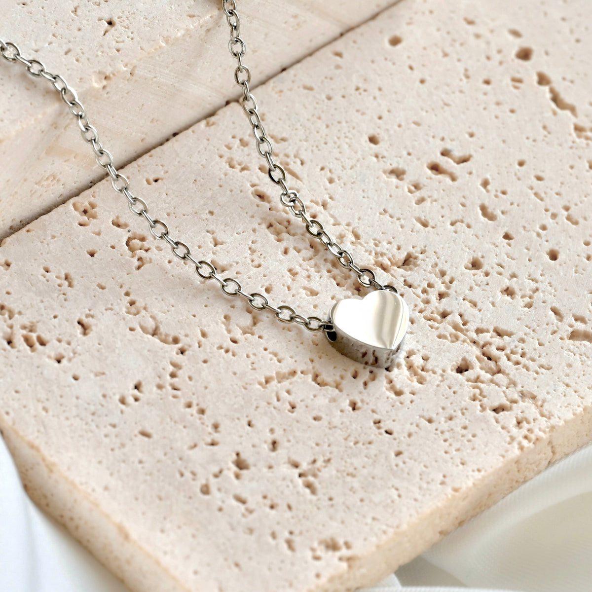 Silver heart necklace on a textured stone surface