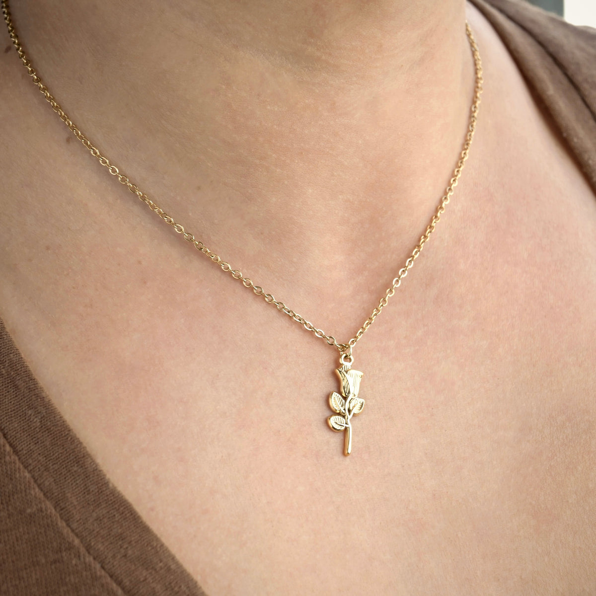 Gold necklace with a rose pendant on a person wearing a brown top.